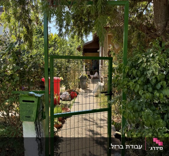 שער מתכת ירוק עם מסגרת פתוח בכניסה לגינה